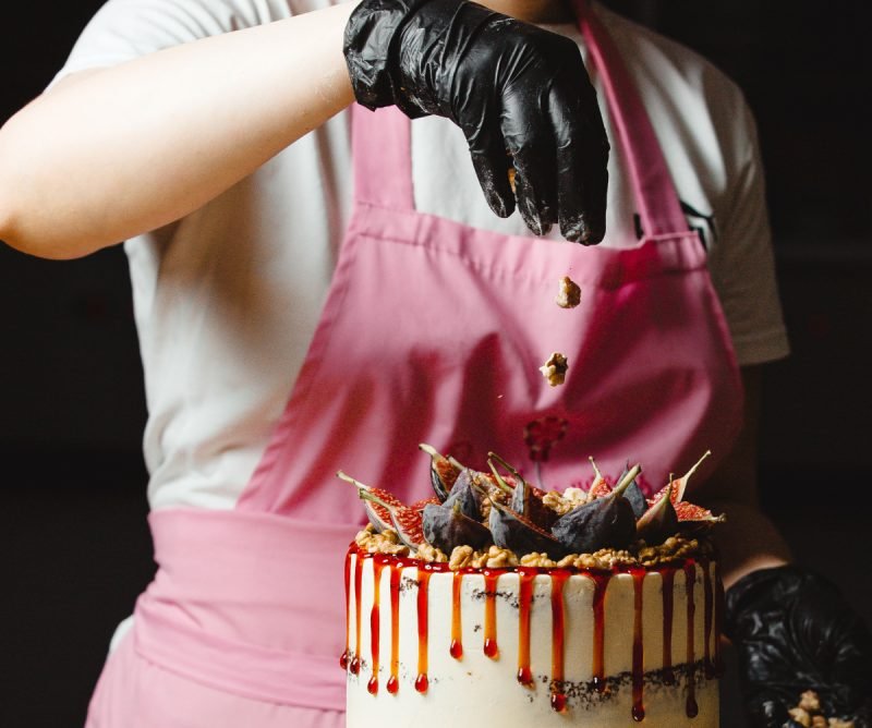 woman-putting-walnut-top-classic-cake-decorated-with-figs-syrup